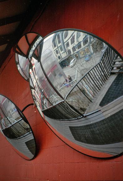On the red wall hang round mirrors that look like glasses. The mirrors reflect the street. 