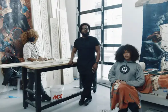 Stephen Hamilton, center, in his studio with the artists Naijah Garrett, left, and Ja’hari Ortega. For the Triennial, Hamilton is preparing carvings and paintings on woven cloth for a large loom installation. Tony Luong for The New York Times