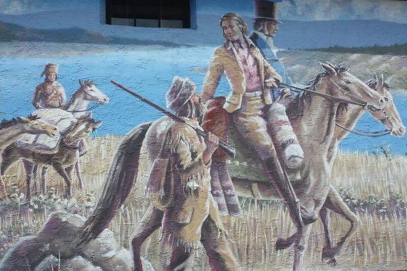 Gentlemen on horseback leading out the brigades, riding past a blue lake. 