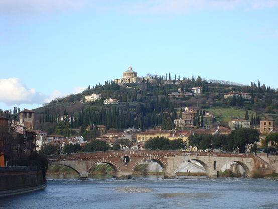A river and a bridge stand in front of a hill with trees and some buildings l. A domed building sits near the top of the hill 