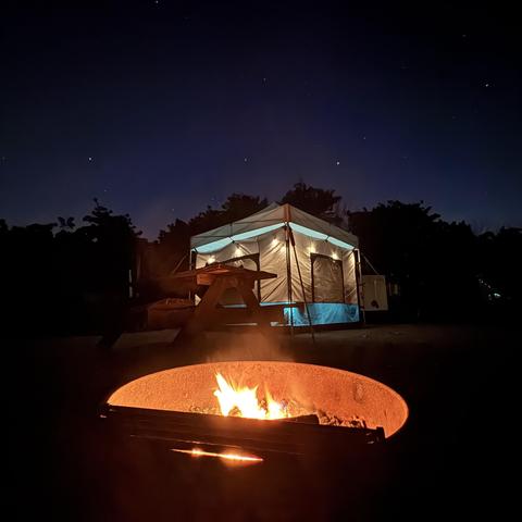 Starry sky over a campsite with a fire and lighted tent.
