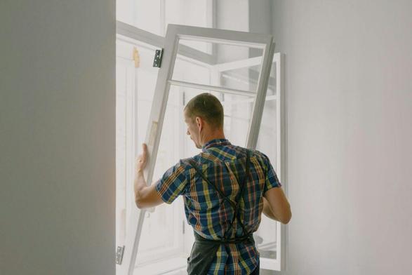 Person in plaid shirt installing a large white window in a brightly lit room