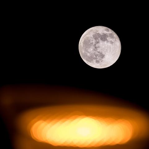 Vollmond über einer unscharf leuchtenden Strassenlaterne. 
