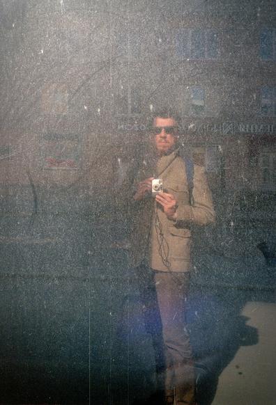 Dusty dark window in which a photographer with a small camera is reflected. Sun, contrasting shadows. 