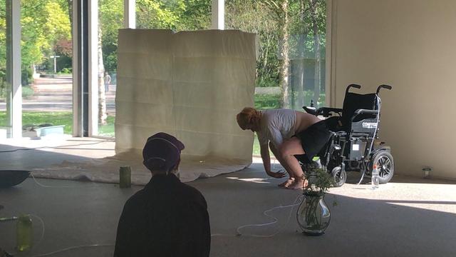 On this picture, we see artist Toni Kritzer crouched in front of their wheelchair in Het Glazen Huis, art space at Zone2Source in Amsterdam. 