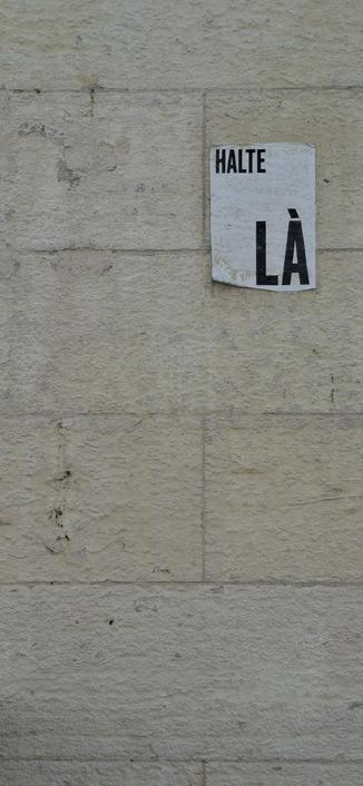 Un mur en pierre d un bâtiment, avec des joints fins, et une feuilles collé dessus avec marqué : "Halte là"