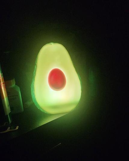 Picture of a dark room with a moderately lit avocado shaped lamp 