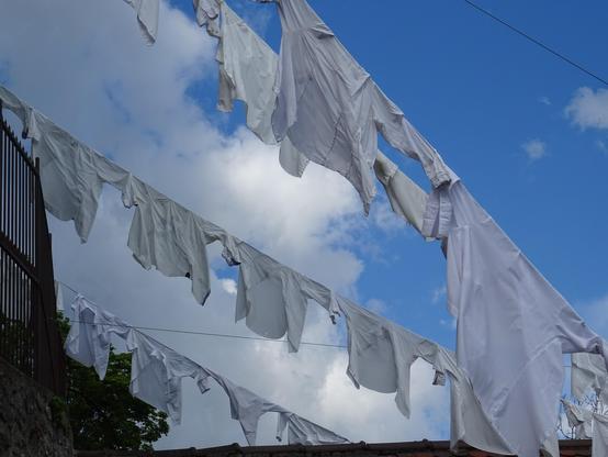 Chemises blanches enfilées par les manche sur des cables. Tout petit détail d'une installation de plein air dénommée "Mon rêve caché". On apperçoit un bout d'arbre, le ciel bleu avec des nuages.
