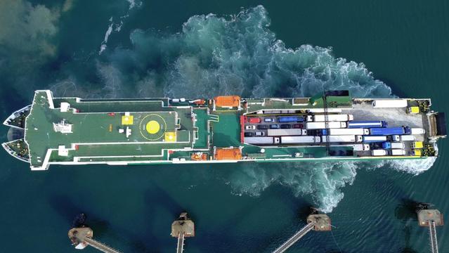 Vertical drone view of a ferry arriving at port. Stern and bow thrusters create a swirl of white water and sediment around the ship.