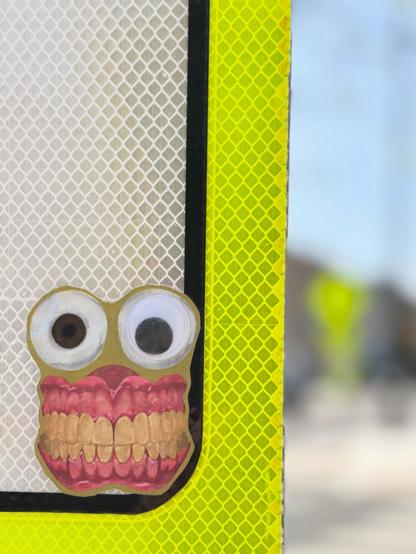Sticker of realistic looking skeleton teeth (with pink gums), with two big round eyes mounted directly atop (think Barbara from Beetlejuice).  I have added one plastic huge googly eye to the right eye. 