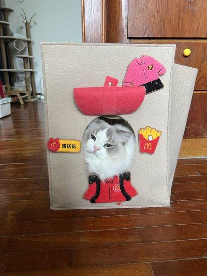 A long haired white and grey cat looking out of a felt looking bag with McDonald’s patches on it