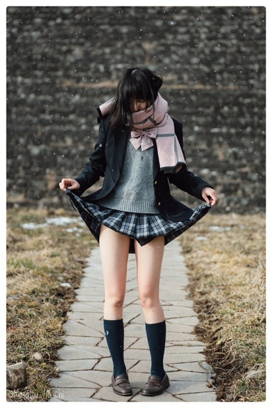 A young woman cosplaying as a Japanese Schoolgirl lifting her skirt giving just a glimpse of her knickers while light slow falls around her