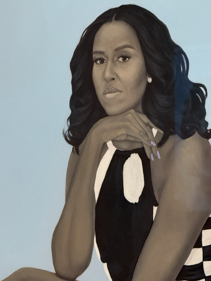 A close-up of Amy Sherrald’s portrait of Michelle Obama—her chin rests on the back of her hand as she gazes ahead. She has shoulder-length black hair, a black-and-white patterned dress. The background is haint blue