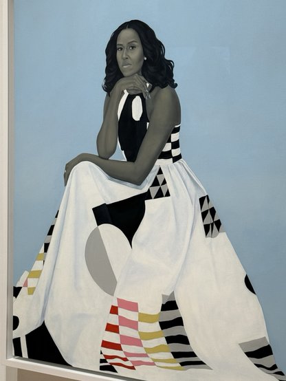 A close-up of Amy Sherrald’s portrait of Michelle Obama—her chin rests on the back of her hand as she gazes ahead. She has shoulder-length black hair, a black-and-white patterned dress. The background is haint blue