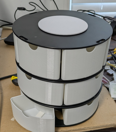 A stack of 3 black plastic spools with white wedge-shaped drawers inserted. One drawer is open, showing a channel along the bottom for a drawer slide.