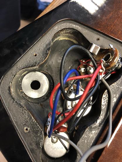 An interior view of an electronic device, featuring various wires (red, white, blue, and black) and components, including metal parts and circular objects, likely related to a guitar or similar instrument.