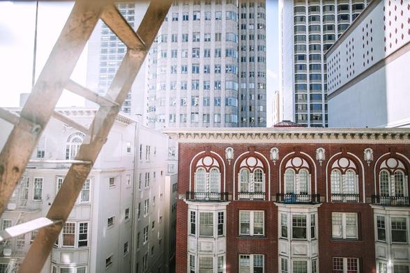 Cityscape view with vintage red brick building framed by modern high-rises and a fire escape ladder in foreground