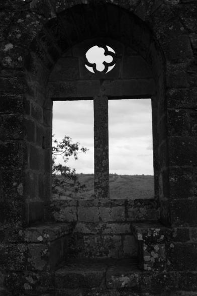 A medieval window, with a landscape outside. Black and white.