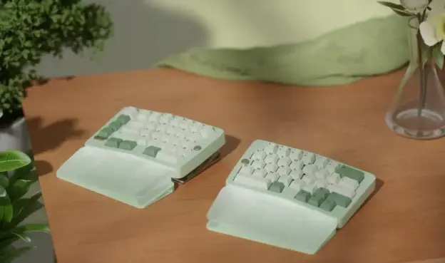 A tented split ergo keyboard in mint green on a wood-grain desk.