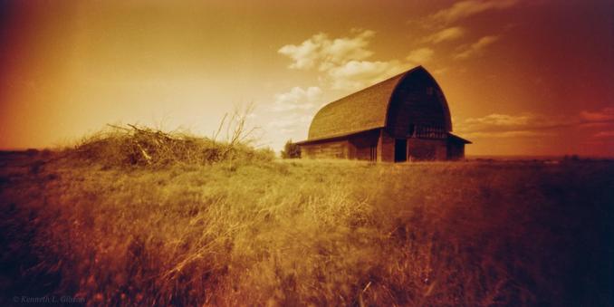 Redscale image of a barn in a field.