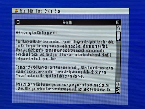 A photograph of a computer monitor, showing an Apple IIgs computer desktop displaying a text file titled "Read.Me"  The text reads:

" *** Entering the Kid Dungeon ***

Your Dungeon Master disk contains a special dungeon designed just for kids.  The Kid Dungeon has many rooms to explore and lots of treasure to find.  When you think you're strong and brave enough, you can hunt a ferocious Dragon.  But, first you'll have to find the hidden key which will let you enter the Dragon's lair

To enter the Kid Dungeon, start the game normally.  When the entrance to the dungeon appears, press and hold down the Option key while clicking the "enter" button on the right hand side of the doorway.

Once inside the Kid Dungeon you can save your game and continue playing later.  When you reload this save game you will not need to hold down the ..."

The text continues further off-screen.