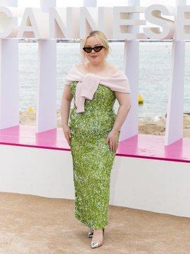 Nicola Coughlan on the beige carpet in a midday cocktail dress. It's formfitting with light green rhinestones all over and goes down to her ankles. She casually wears a light pink sweater around her bare shoulders, silver pumps, her hair in a messy bun and black sunglasses.