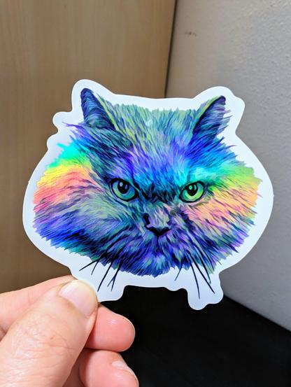 Photo of a left hand holding a diecut sticker. The sticker is a holographic grumpy Persian cat drawing.
