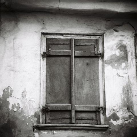 Black and white photo of shuttered window in the distressed wall of an old medieval house.