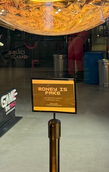 A plastic sphere half-filled with cash suspended from the ceiling. A sign says “money is fake/for entertainment purposes only “