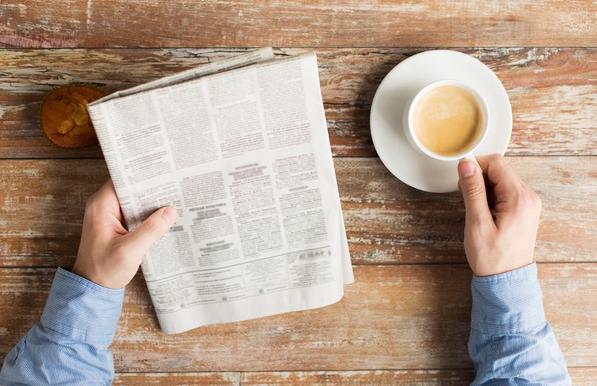 A view from above of a person reading a newspaper and drinking a cup of coffee. Image by Ground Picture via Shutterstock.