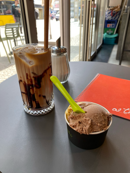 Iced latte and extra ice cream in a cup on a plain cafe table, orange menu says “al teatro”