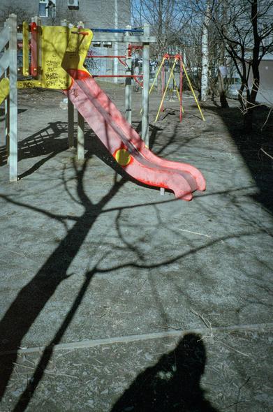 Multicolored children's playground: slide, swings. Contrasting shadows of a tree and a photographer fall on the playground. 