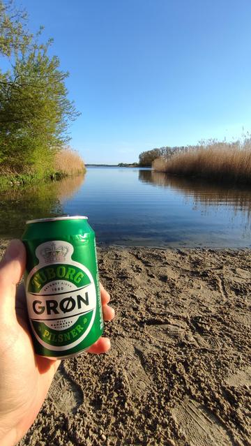 Foto. Tuborg-Dose, dahinter ein ruhiger See am Abend.