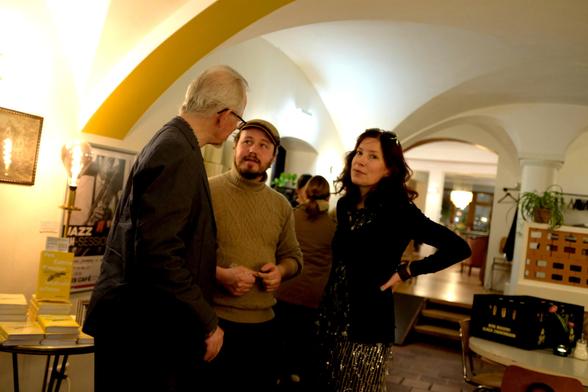 Verleger Thomas Zehender, Aegis-Inhaber Rasmus Schöll und Autorin Fee Kanzler nachts im Ulmer Aegis Café, gemeinsam ins Gespräch vertieft. Fee wirft einen Seitenblick in Richtung Fotograf.