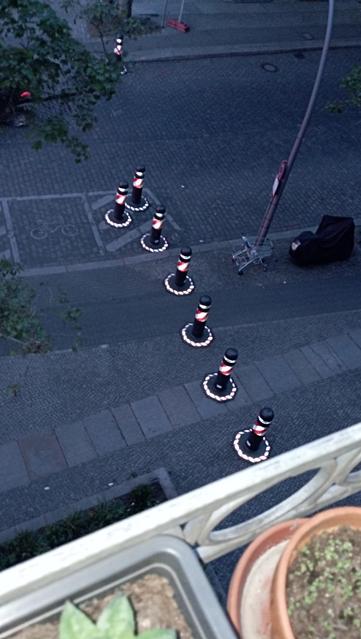Schnappschuss vom Balkon:
8 Poller, 
Mit rot-weißer Warn-Schraffur mittig & an der Bodenplatte 
Neben der Straße (Kopfsteinpflaster - Fahrbahn) bereitgestellt 