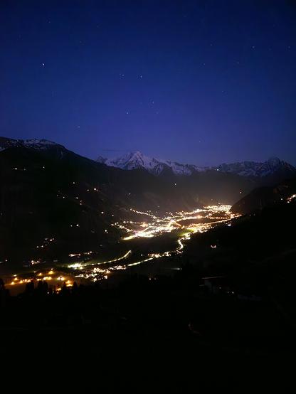 Blick von einer Berg Flanke ins hinter Zillertal. Es ist fast schon dunkel und die Lichter der Straßen und Häuser stralen. Erste Sterne sind zu sehen am Himmel. Die Berge im Hintergrund sind noch schneebedeckt.