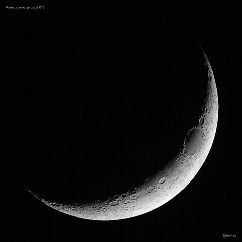 Gray lunar crescent roughly banana-thick with horns pointing to the upper left against fully black background. Dark smooth mare crisium is prominent on the terminator with the peaks of its rim already lit beyond the terminator.