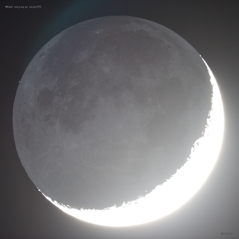 Full lunar disk against hazy background. The actual lit crescent appears fully white and overexposed to the lower right. Mare and ray systems as they appear on the full moon are visible on the dark side but here illuminated only by reflected light from Earth. To the upper right the magnitude 8 star HD 35586 appears as a small white dot about a minute before being occulted.