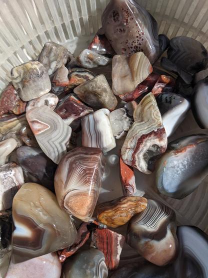 A pile of cool rocks in the sunshine. Like, really cool rocks, in shades of white, grey, brown and red orange, with prominent stripes on almost all of them in similar shades.