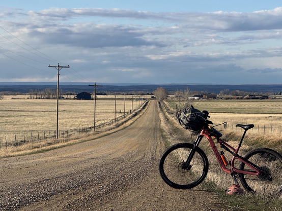 Pink mountain bike on a long, gravel road under blue skies with white clouds
