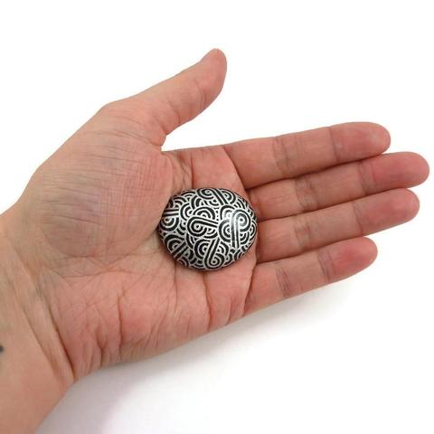 Magnet unique réalisé avec un faux galet ovale en FIMO, peint en noir et recouvert de volutes argentées.