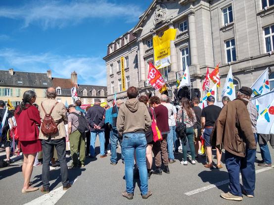 Une foule vide dos. Sur la droite de la photo, il y a une voiture sono avec des drapeaux syndicaux.
Sur le fronton de la mairie, il y a un immense maillot jaune avec écrit "Guéret ville arrivée du tour de France femme" et une autre banderole jaune marquée "30 juillet"