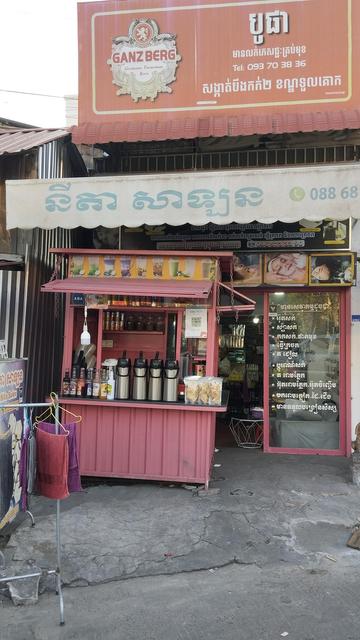 A small pink iced drink shop in front of a house. The different flavours are displayed as images on the top.