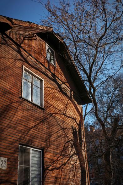 The photo shows a wooden house being shaded by a neighboring tree. 