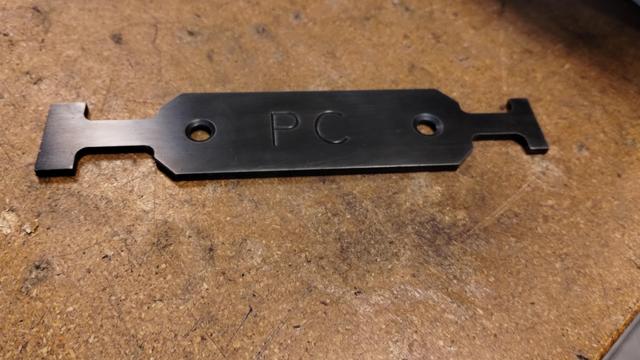 a metal T slot cleaner sitting on a table. it has a blued finish.