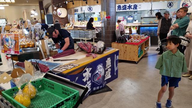 My wider-angled photograph of a takumi demonstrating the art of cutting up an entire skipjack tuna, with a curious boy on-looking.