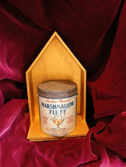 An antique tin can of Marshmallow Fluff. It says Durkee-Mower's brand, and it has what looks like a fruit cocktail in a dessert glass with fluff on top. So obviously it was good for you--you know, fruit. 

It has a screw-on tin lid with embossed FLUFF on that too. 

The little can maybe 4 inches tall sits in a little wooden platform kind of like a sconce with a pointed peak. That sits in a plush red velvet case.