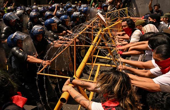 Protesters clash with the police during a Labor Day demonstration in Manila, across a barbwire scaffolding.