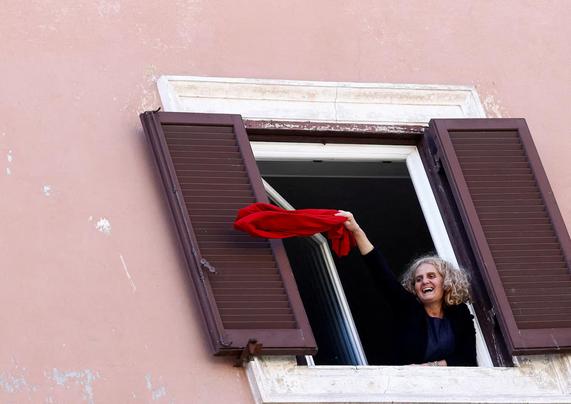 An elderly woman waves a red cloth from her window.