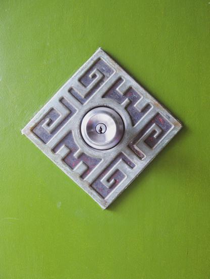 A doorknob on a lime green surface. The door knob is decorated with some intricate carvings around it.